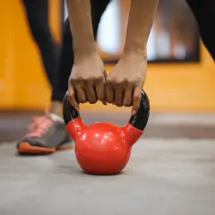 Dłonie trzymające czerwoną kettlebell na siłowni.