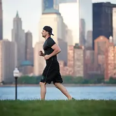 Mężczyzna w czapce i stroju sportowym biegnie na tle panoramy miasta i wody.