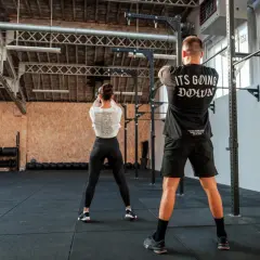 Para trenująca CrossFit w siłowni, wykonująca ćwiczenie z kettlebell.