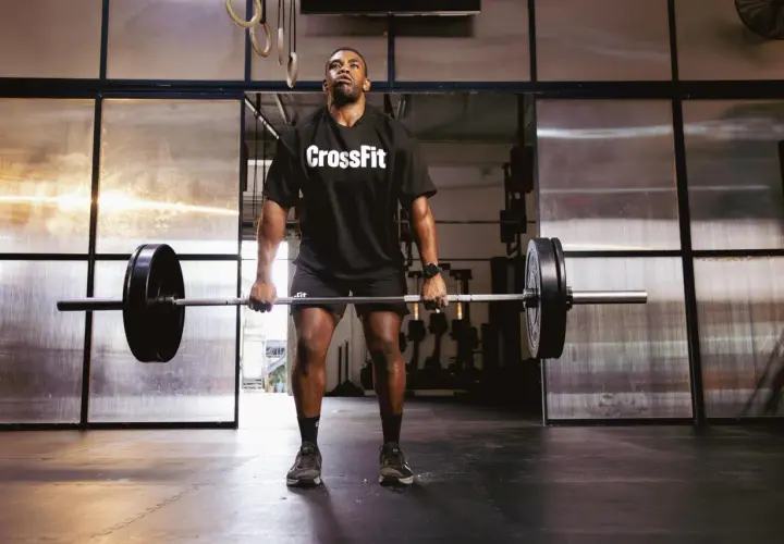 Mężczyzna w koszulce CrossFit podnosi sztangę na siłowni.