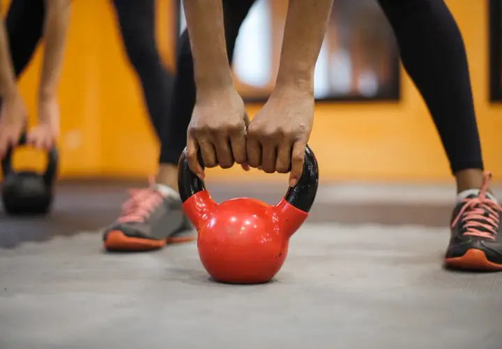 Dłonie trzymające czerwoną kettlebell na siłowni.