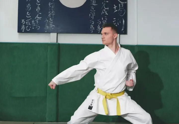 Mężczyzna w białym karate gi z żółtym pasem w pozycji bojowej.