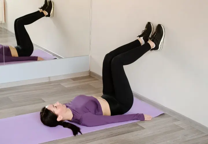 Kobieta ćwiczy pilates, leżąc na macie z nogami opartymi o ścianę.