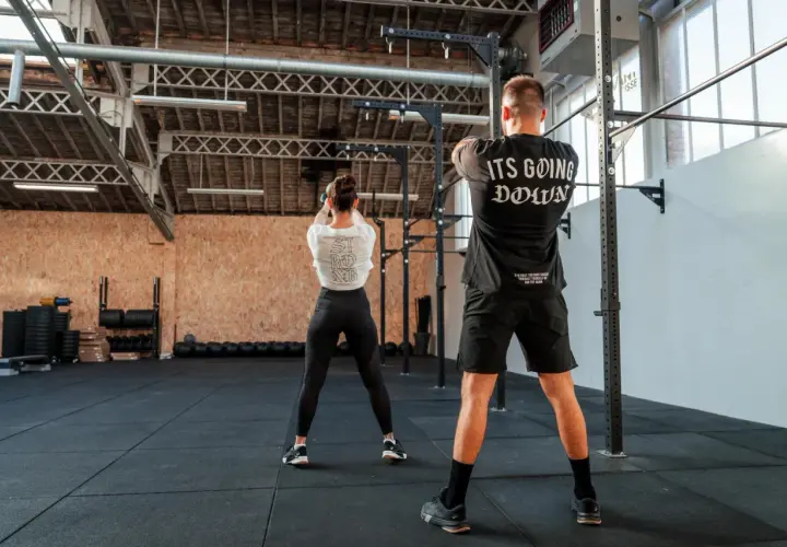 Para trenująca CrossFit w siłowni, wykonująca ćwiczenie z kettlebell.