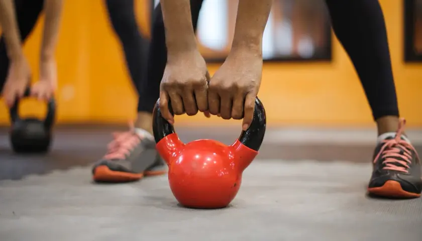 Dłonie trzymające czerwoną kettlebell na siłowni.