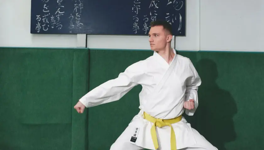 Mężczyzna w białym karate gi z żółtym pasem w pozycji bojowej.