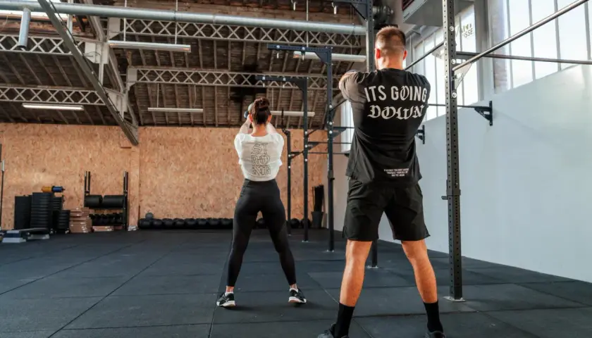 Para trenująca CrossFit w siłowni, wykonująca ćwiczenie z kettlebell.
