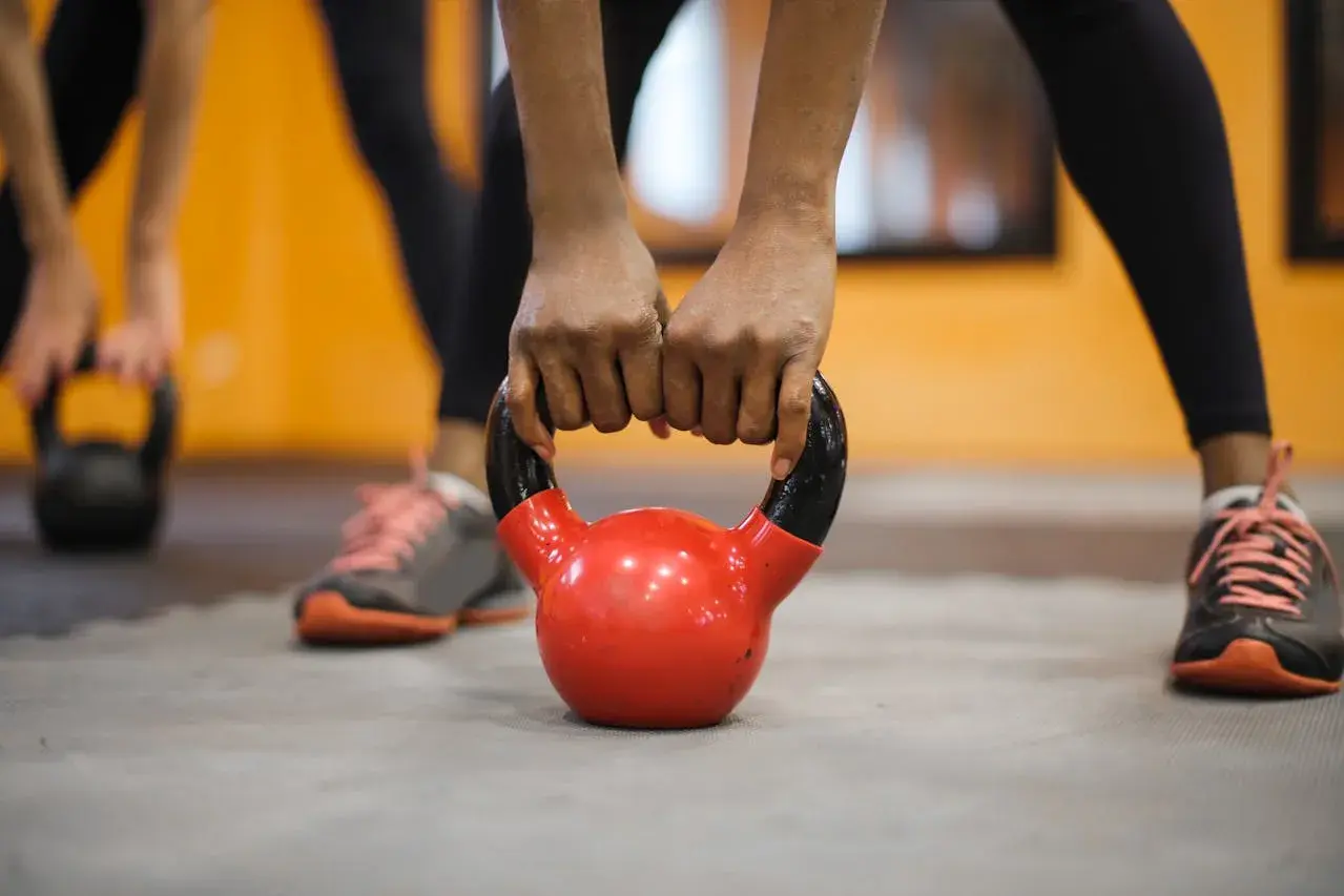 Dłonie trzymające czerwoną kettlebell na siłowni.