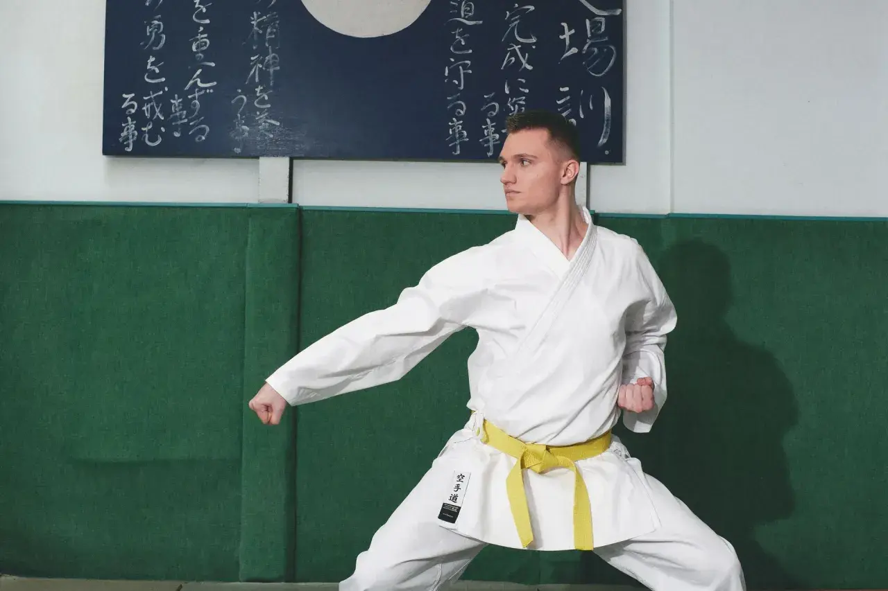 Mężczyzna w białym karate gi z żółtym pasem w pozycji bojowej.