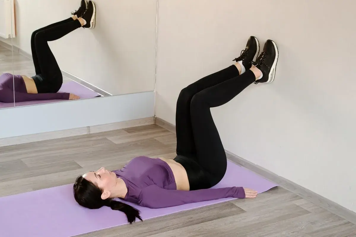 Kobieta ćwiczy pilates, leżąc na macie z nogami opartymi o ścianę.