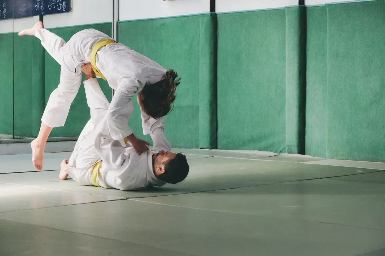 Dwie osoby w judogach ćwiczą rzuty. Judo to jeden ze sportów walki na olimpiadzie.