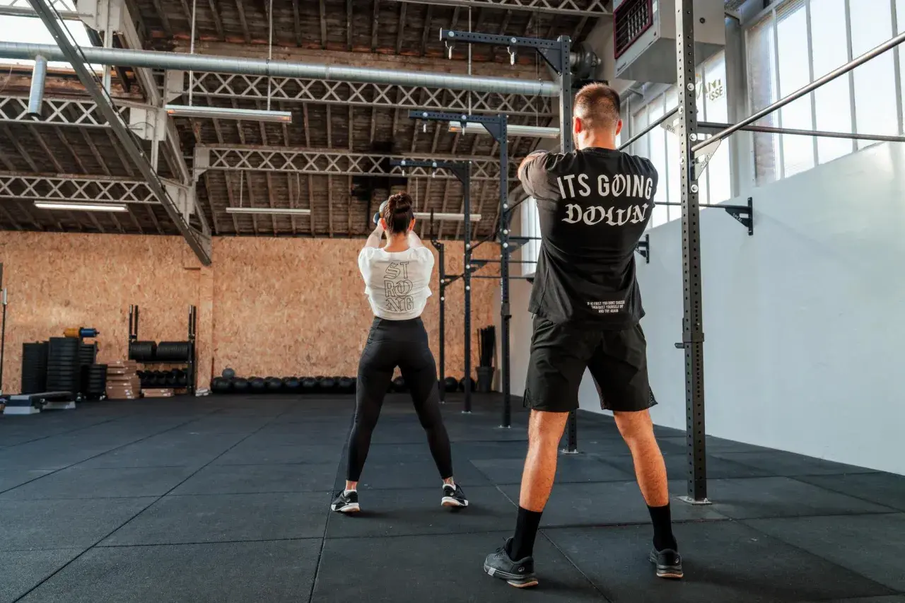 Para trenująca CrossFit w siłowni, wykonująca ćwiczenie z kettlebell.