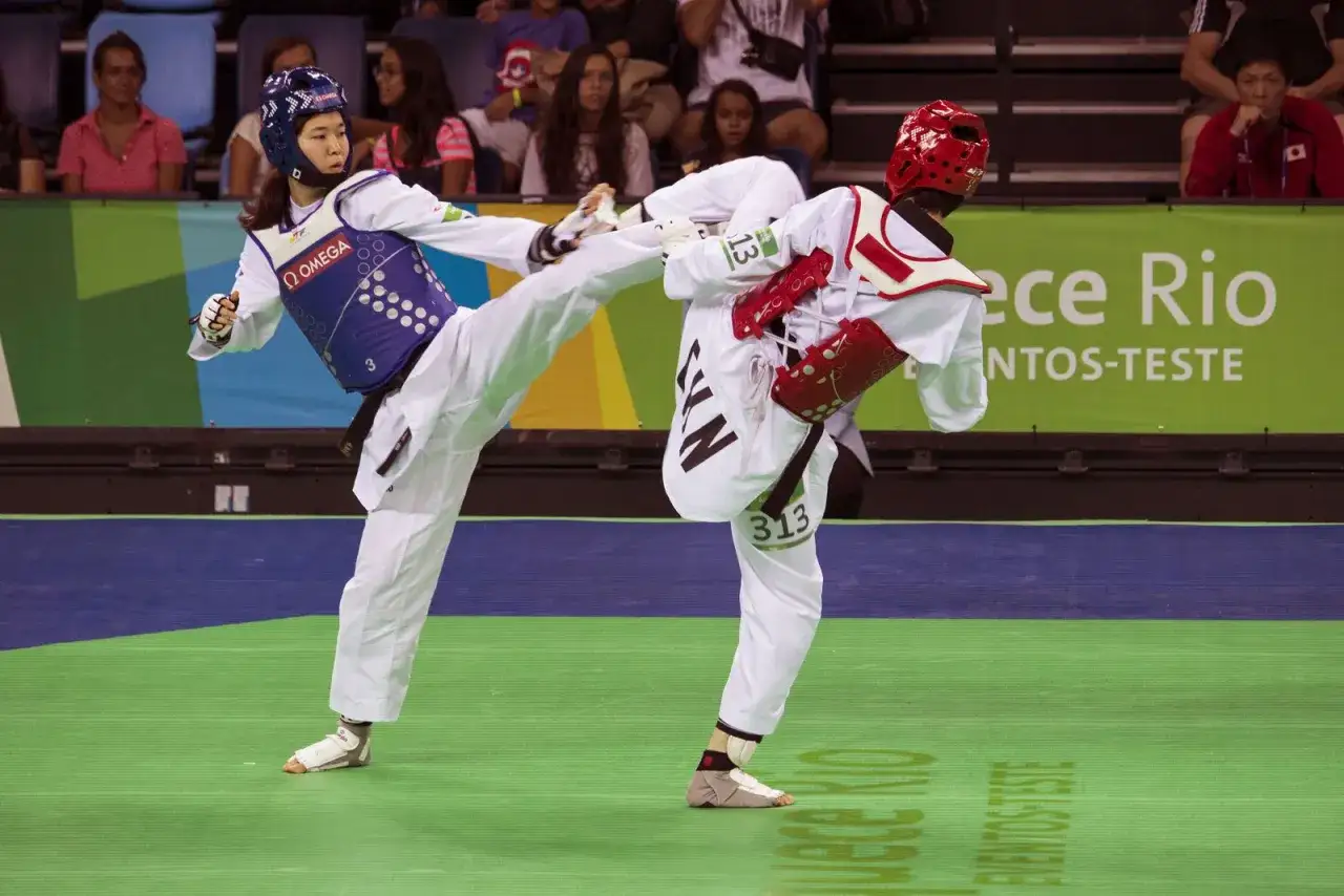 Zacięta walka taekwondo, jednego ze sportów walki na olimpiadzie. Zawodniczka wykonuje wysokie kopnięcie.